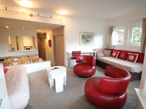 Un salon moderne avec un canapé, des fauteuils rouges, une table basse blanche et un coin repas comprenant une table et des chaises.