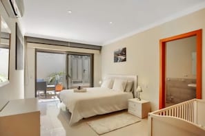A bedroom with a bed, bedside table, and a crib. There is a sliding glass door leading to a balcony with a chair and a potted plant. - Belvilla by OYO Holiday home in Puerto de Santiago (Puerto de Santiago)
