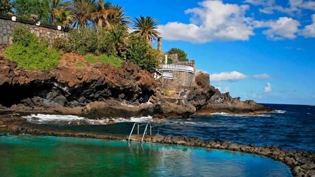 A coastal scene with a clear pool, rocky shoreline, and a building with a white railing.