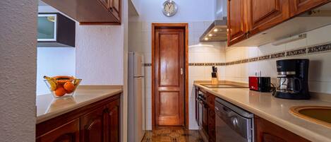 A kitchen with wooden cabinets, a tiled backsplash, a refrigerator, a coffee maker, and a bowl of fruit on the counter.