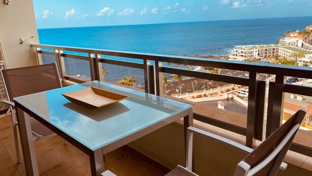 Un balcón con mesa y sillas de vidrio que da a vistas de la costa.