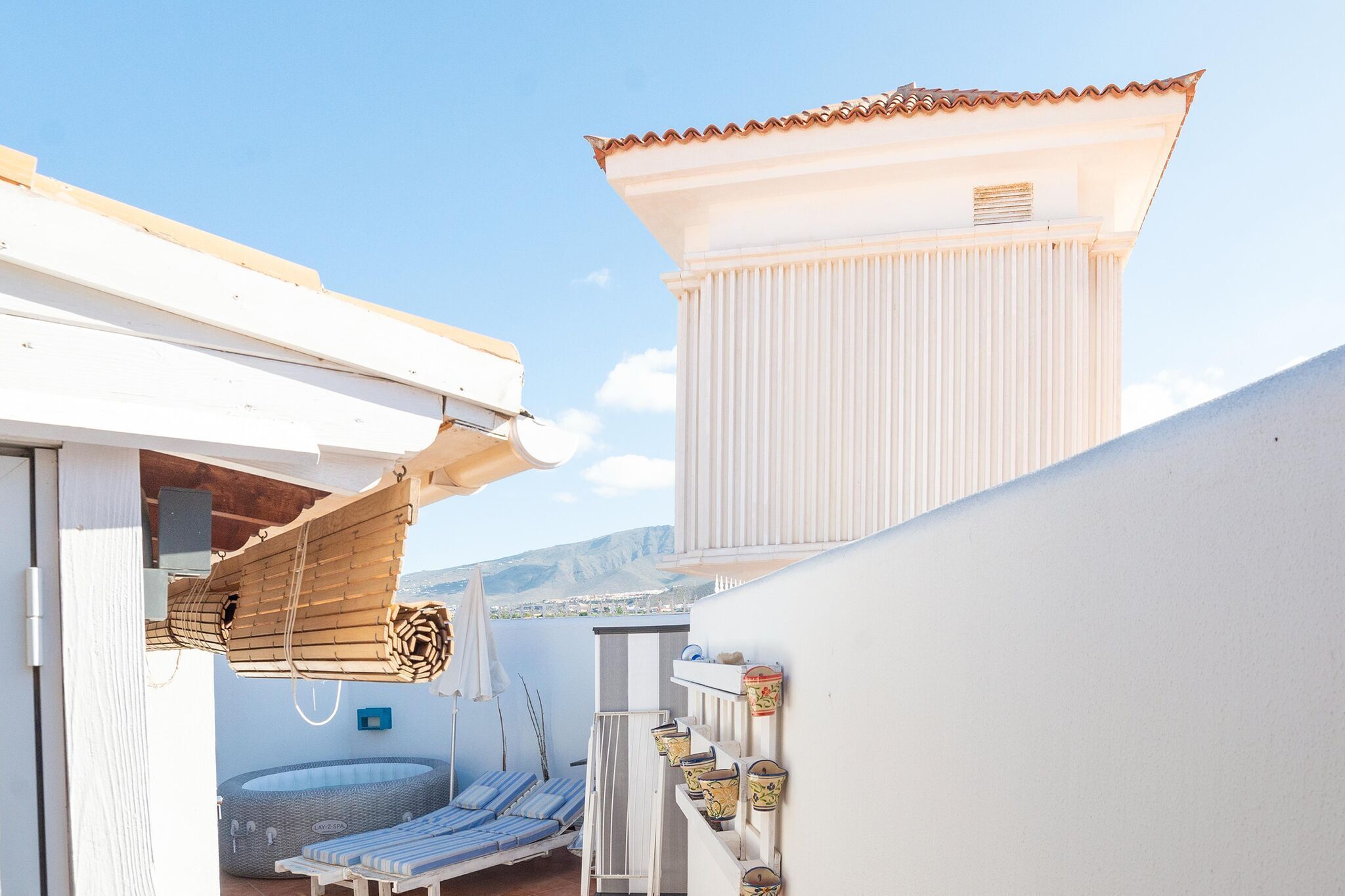 A rooftop terrace with a sun lounger, a small pool, and a view of the surrounding landscape.