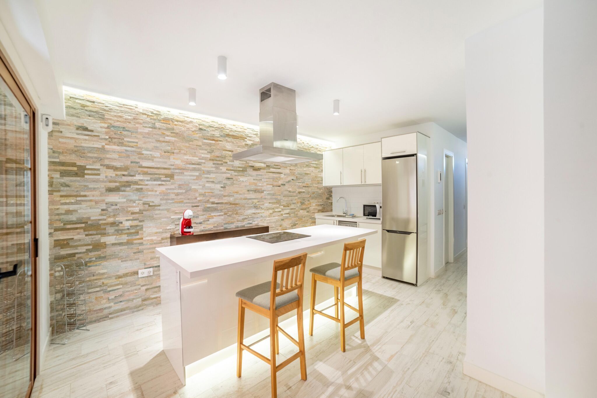 Een moderne keuken met een betegelde achterwand, roestvrijstalen apparatuur en een centraal kookeiland met twee houten barstoelen.