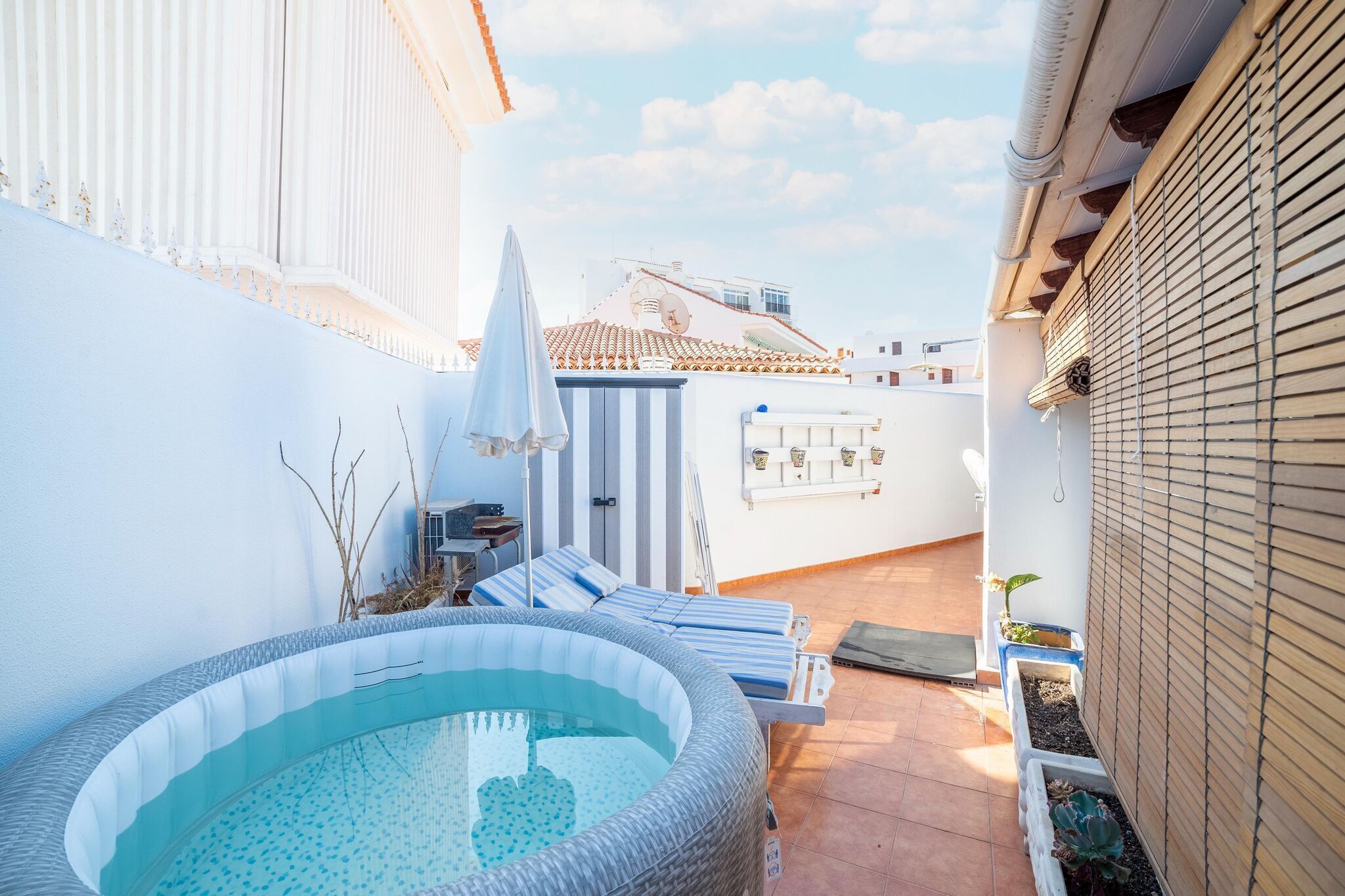 Un área de piscina en la azotea con sillones, un jacuzzi y plantas en macetas.