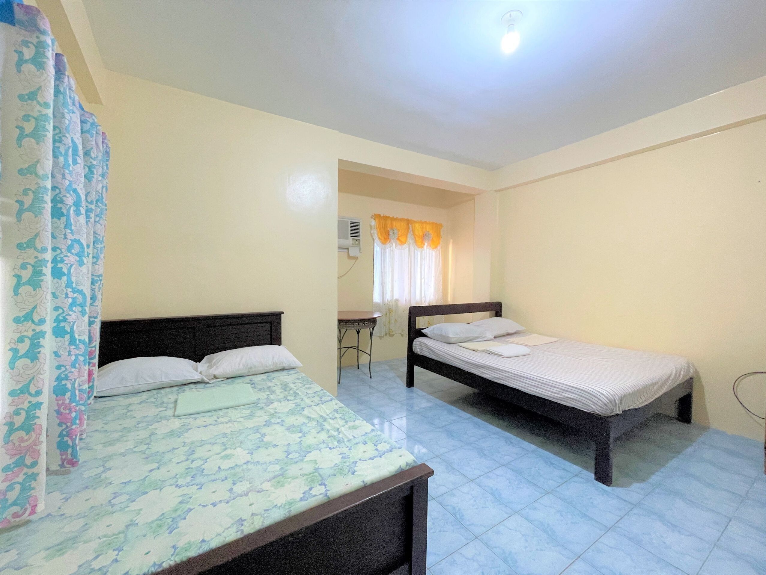 A room with two beds, a small table, and a window with curtains.