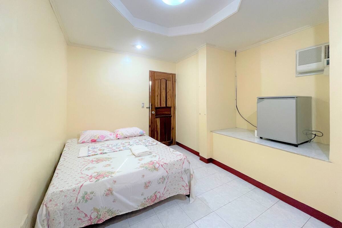 Une chambre à coucher avec un lit, une porte en bois, un climatiseur blanc et une petite fenêtre.