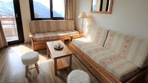 A cozy living room with a sofa, a small table, and a chair. There is a window with a view of mountains. - Avoriaz - 2-room Apt, 6 pers, village view, WiFi (Avoriaz)