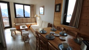 A cozy dining area with a wooden table set for four, a sofa, and a window with a view of mountains. - Avoriaz - 2-room Apt, 6 pers, village view, WiFi (Avoriaz)