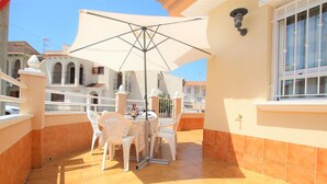 A balcony with a table and chairs, a large umbrella, and a tiled floor.
