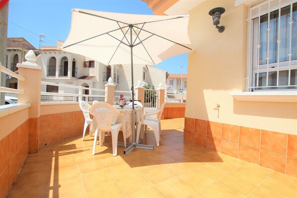 A balcony with a table and chairs, a large umbrella, and a tiled floor.
