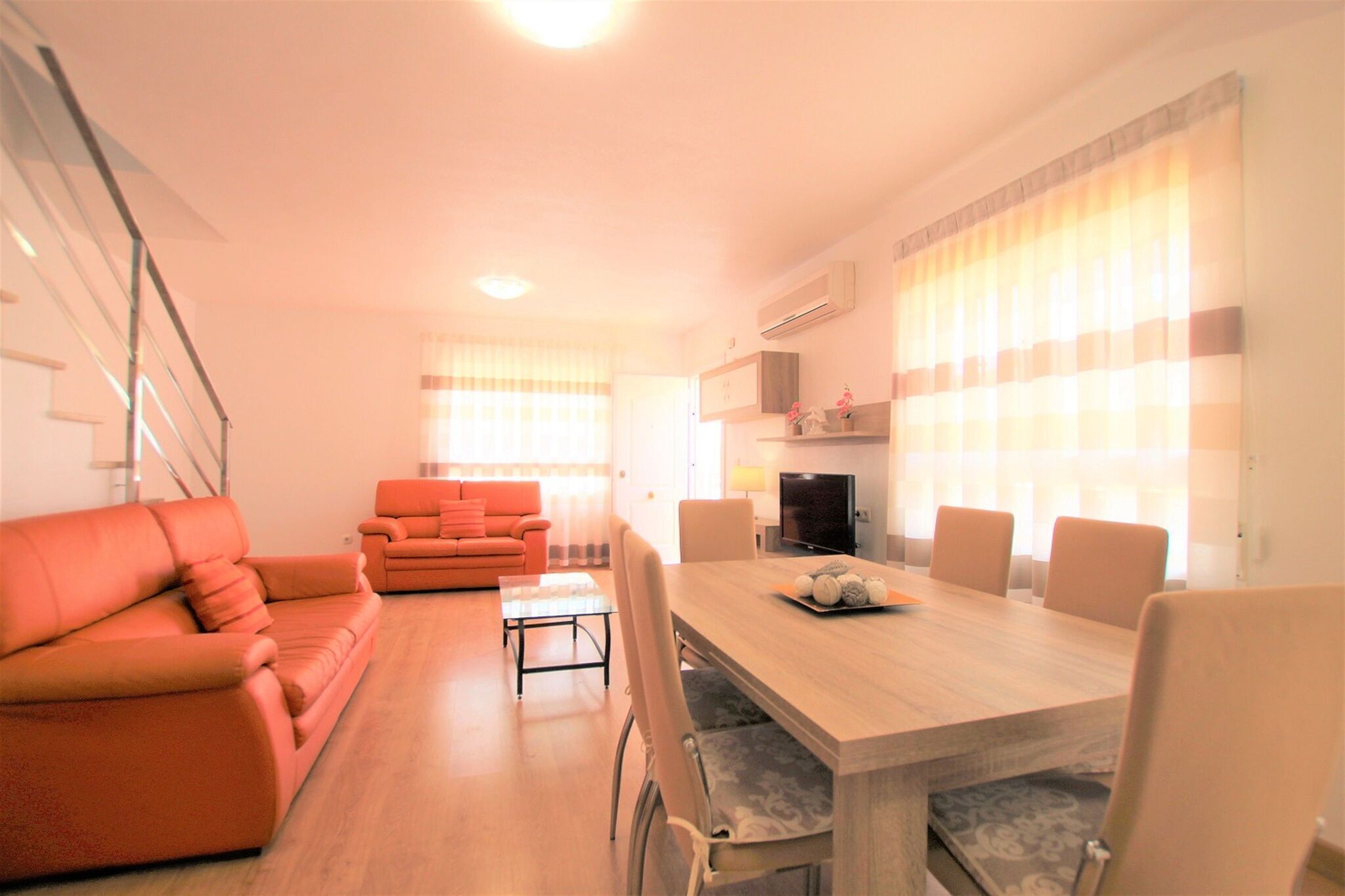 Una sala moderna con una mesa de comedor de madera, sofás naranja y un televisor.