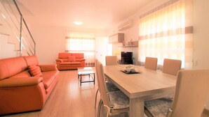 A modern living room with a wooden dining table, orange sofas, and a TV.