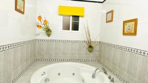 Un baño con bañera, una ventana con persiana amarilla y cuadros en las paredes.