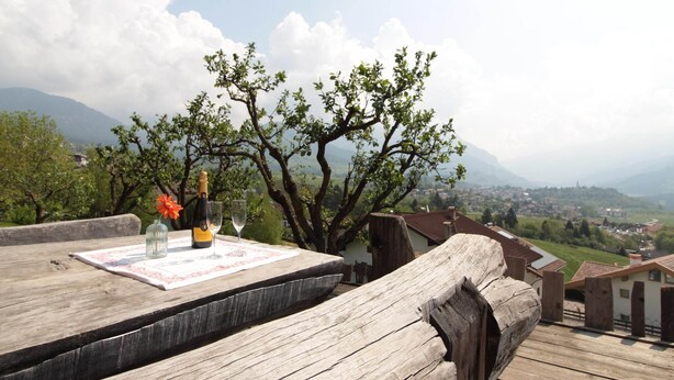 A wooden deck with a bottle and glass, overlooking a town and mountains.