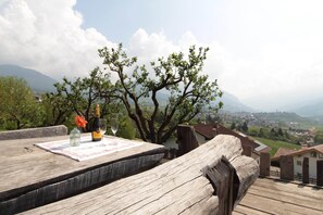 A wooden deck with a bottle and glass, overlooking a town and mountains.