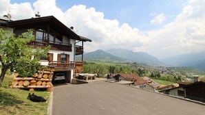 A two-story building with a balcony, a wooden deck, and a view of a valley and mountains.