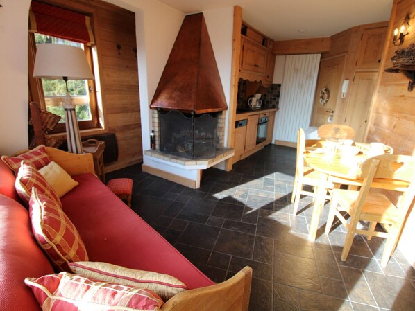 A cozy living room with a red sofa, a fireplace, a dining area with a wooden table and chairs, and wooden cabinetry.
