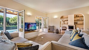 A spacious living room with a large TV, comfortable seating, a fireplace, and a view of the outdoors. - Large villa with swimming pool within walking distance to the beach (Castro Marim)