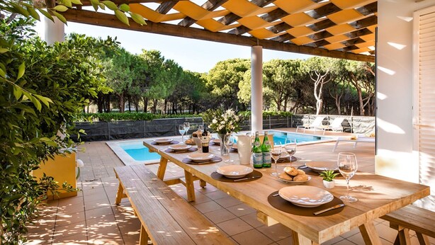 A wooden outdoor dining area with a pool in the background. - Large villa with swimming pool within walking distance to the beach (Castro Marim)
