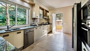 A modern kitchen with a dishwasher, stove, and large windows overlooking a garden. - Large villa with swimming pool within walking distance to the beach (Castro Marim)