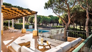 A poolside area with a pergola, lounge chairs, a wooden bench, and a view of a pool and trees. - Large villa with swimming pool within walking distance to the beach (Castro Marim)