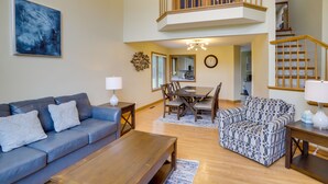 A spacious living room with a blue sofa, a patterned armchair, a wooden coffee table, and a dining area with a wooden table and chairs.