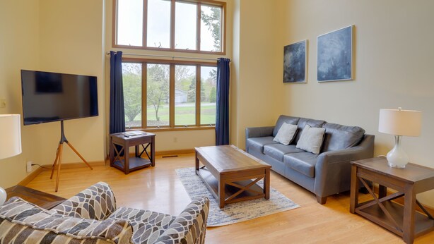 A living room with a flat-screen TV, a grey sofa, a wooden coffee table, and a lamp on a side table.