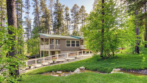 A cabin with a deck, surrounded by a forest and a small stream.