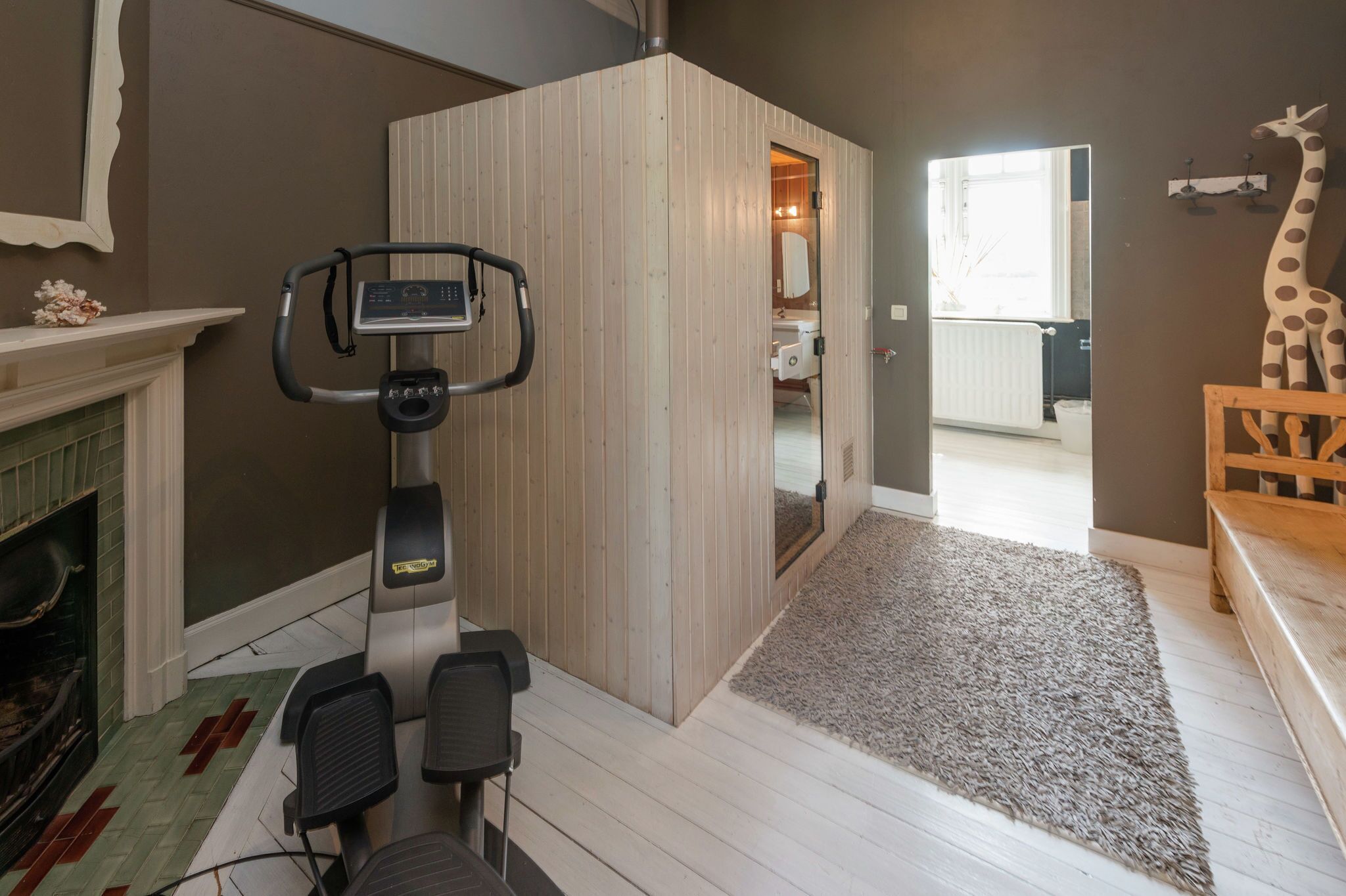 A room with a stationary bike, a fireplace, a wooden partition, and a giraffe decoration.