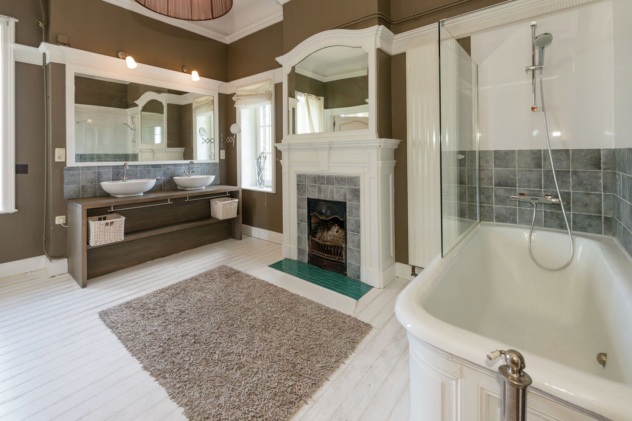 A bathroom with a large bathtub, a fireplace, and a double sink with a mirror above.