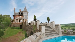 Un edificio grande e histórico con piscina, escalones de piedra y vistas al campo.