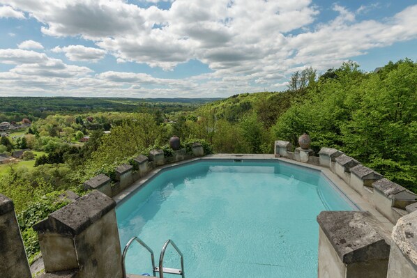 Una piscina rectangular con borde de piedra, rodeada de abundante vegetación y un cielo despejado.