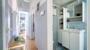 A hallway with a wooden floor leading to a bathroom with a white sink and blue tiles. - Snug apartment in Αθήνα with veranda (Αθήνα)