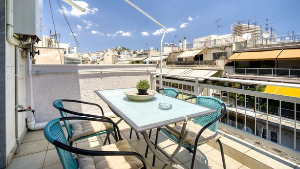 A rooftop terrace with a table and chairs, a potted plant, and a view of the cityscape. - Snug apartment in Αθήνα with veranda (Αθήνα)