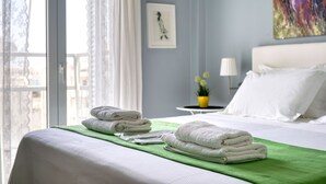 A hotel room with a neatly made bed, a green towel on the bed, a small table with a lamp, and a window with curtains. - Snug apartment in Αθήνα with veranda (Αθήνα)