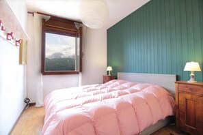 Une chambre à coucher avec un lit, une fenêtre donnant sur les montagnes, une table de chevet en bois et une lampe fixée au mur.