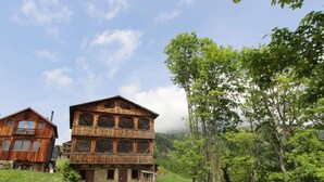 A rustic wooden building with multiple windows and balconies, surrounded by lush greenery and trees.
