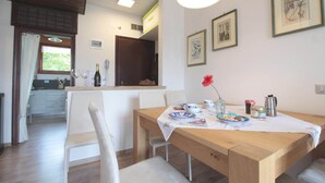A dining area with a wooden table, white chairs, and a kitchen in the background.