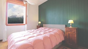 A bedroom with a bed, two bedside tables with lamps, a window with curtains, and a view of mountains.