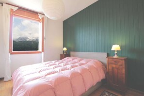 A bedroom with a bed, two bedside tables with lamps, a window with curtains, and a view of mountains.