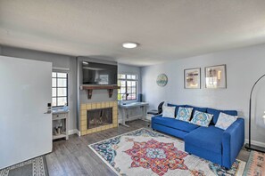 A living room with a blue sofa, a fireplace, a desk, and a large rug. - Breezy Monterey Apt: Walk to Downtown & Beach (Monterey)