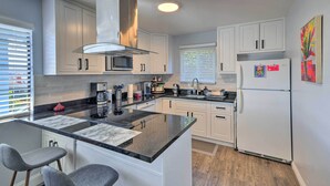 A modern kitchen with white cabinets, a central island with bar stools, a stainless steel range hood, and a refrigerator with magnets. - Breezy Monterey Apt: Walk to Downtown & Beach (Monterey)