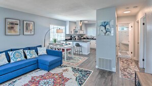 A modern living room with a blue sofa, patterned rugs, and a kitchen in the background. - Breezy Monterey Apt: Walk to Downtown & Beach (Monterey)