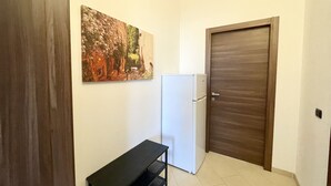 Ein kleiner, sauberer Raum mit einem weißen Kühlschrank, einer Holztür und einem Bild an der Wand.