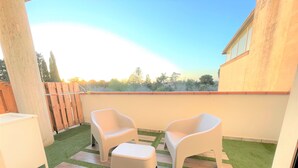 Eine Terrasse mit zwei weißen Stühlen und einem kleinen Tisch, umgeben von Kunstgrün und Holzdeck.