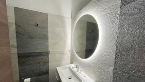 Ein modernes Badezimmer mit einem großen Spiegel, einem weißen Waschbecken und einer Duschkabine.