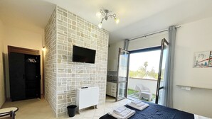 Ein Schlafzimmer mit Bett, Kleiderschrank, Fernseher, einer kleinen Küchenzeile und einer Glastür zum Balkon.