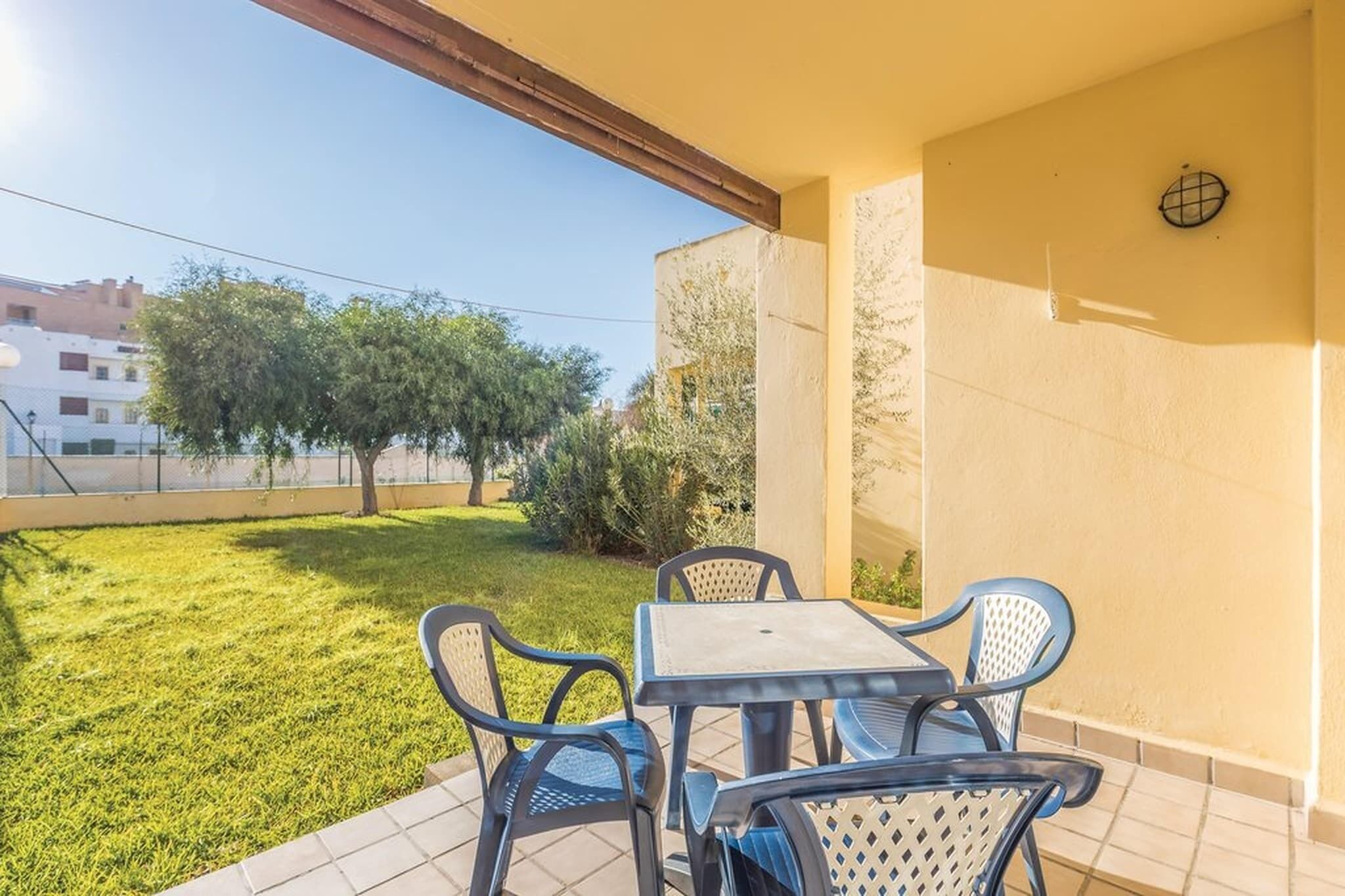 A patio with a table and chairs, a small garden, and a view of buildings in the background.