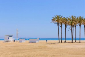 A beach with palm trees, a lifeguard tower, and a small building. - Apartment in Roquetas near Sea Beach (Roquetas de Mar)