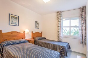 Ein Schlafzimmer mit zwei Betten, einem Nachttisch, einer Lampe und einem Fenster mit Vorhängen.